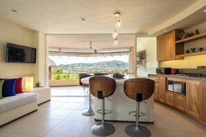 Enjoy meals and entertainment in this spacious kitchen and dining area, featuring a central island with bar stools, a flat-screen TV, and a stove.