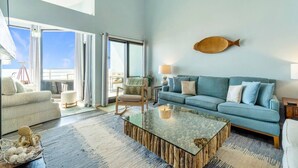 A spacious living room with a large sofa, a glass coffee table, and a view to the outside.