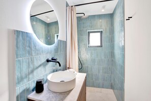 Features a large mirror, sleek sink, and modern faucet, with a glass shower enclosure and blue-tiled walls.