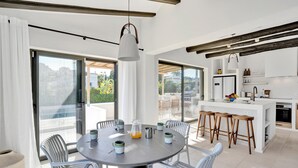 A modern kitchen with white cabinetry, a central island with stools, and large windows offering a view of the outdoors. - Jujube - Javea, Costa Blanca (Javea)