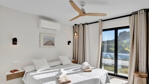 A modern hotel room with a large bed, ceiling fan, air conditioning unit, and a view of the outdoors. - Jujube - Javea, Costa Blanca (Javea)