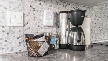 A kitchen with a coffee maker, a kettle, and a basket of dishes.