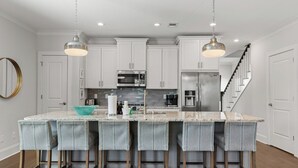 A kitchen with white cabinets, a central island with bar stools, and stainless steel appliances. - Private Pool + 6  ppl Golf Cart - Blue Mtn. Beach (Santa Rosa Beach)