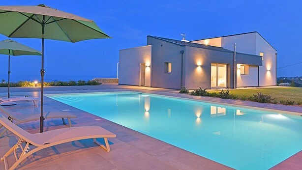 A modern building with a swimming pool, lounge chairs, and umbrellas. - Villa Brezza: A bright and sunny three-story villa situated in a quiet location, a few minutes from the town center, with Free WI-FI. (Giarre)