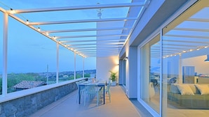 A covered outdoor balcony with a dining table and chairs, large windows, and a view of the landscape. - Villa Brezza: A bright and sunny three-story villa situated in a quiet location, a few minutes from the town center, with Free WI-FI. (Giarre)