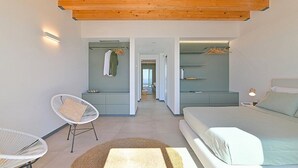 A modern bedroom with a large bed, a seating area with chairs, a walk-in closet, and a hallway leading to another room. - Villa Brezza: A bright and sunny three-story villa situated in a quiet location, a few minutes from the town center, with Free WI-FI. (Giarre)