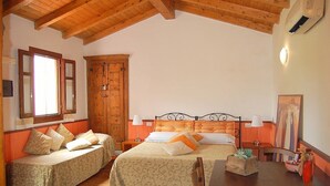 A bedroom with two beds, wooden ceiling beams, a wooden wardrobe, and a dining table with chairs.