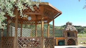 A wooden gazebo with lattice sides and a stone oven.
