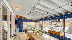 Un'area pranzo coperta con tavolo in legno, sedie e piante in vaso.