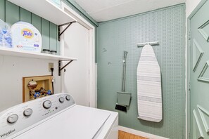 Vaskerum med en Whirlpool vaskemaskine, Tide vaskemiddel og et hængende strygejern.