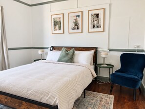 A neatly arranged bedroom with a bed, bedside tables, a chair, and wall-mounted artwork. - 4BR Central Dubbo Family Home, 2 Living Areas, Large Backyard, Sleeps 8 (Dubbo)