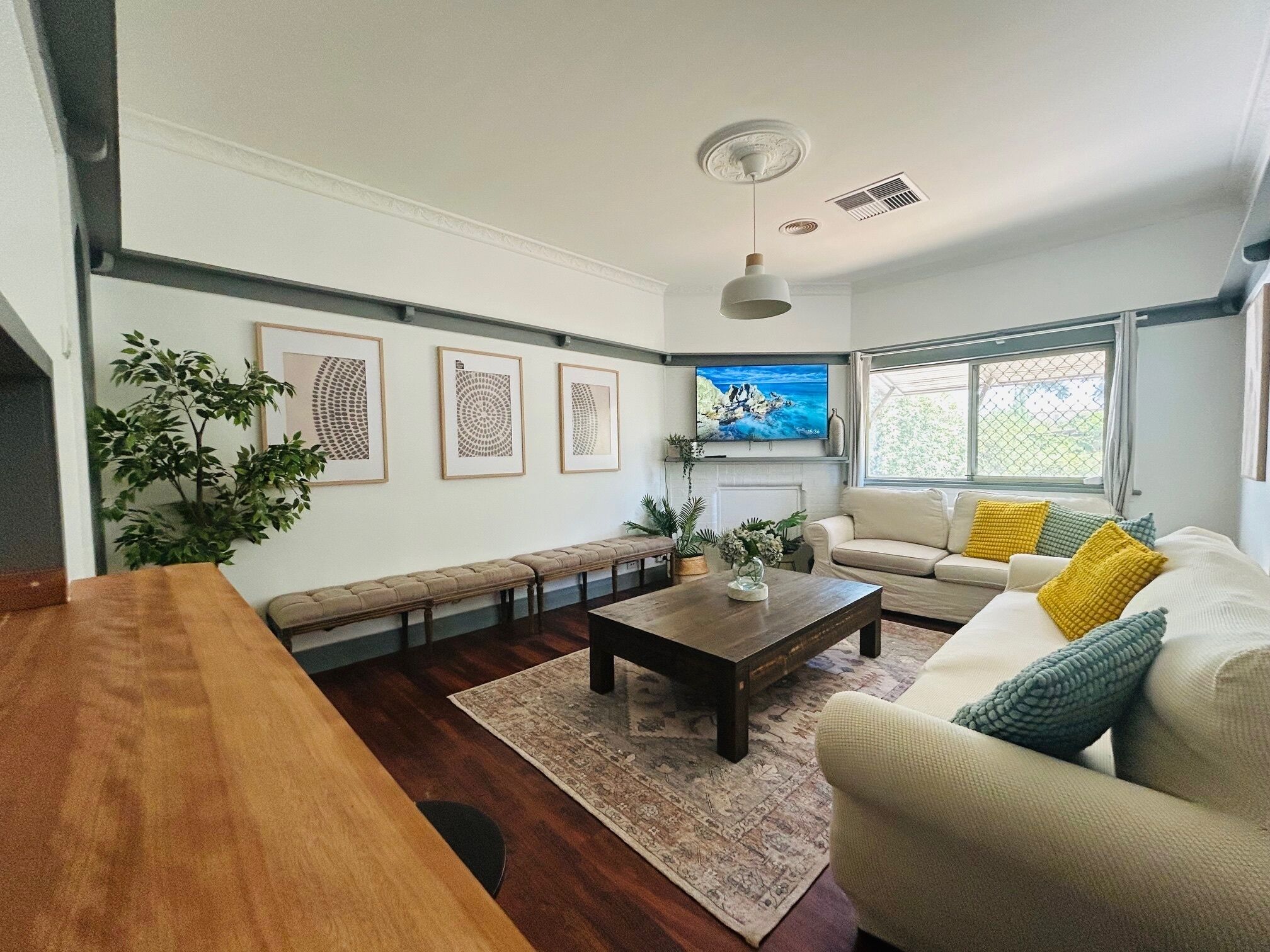 A living room with a wooden bench, a sofa with cushions, a coffee table, and framed artwork on the wall.