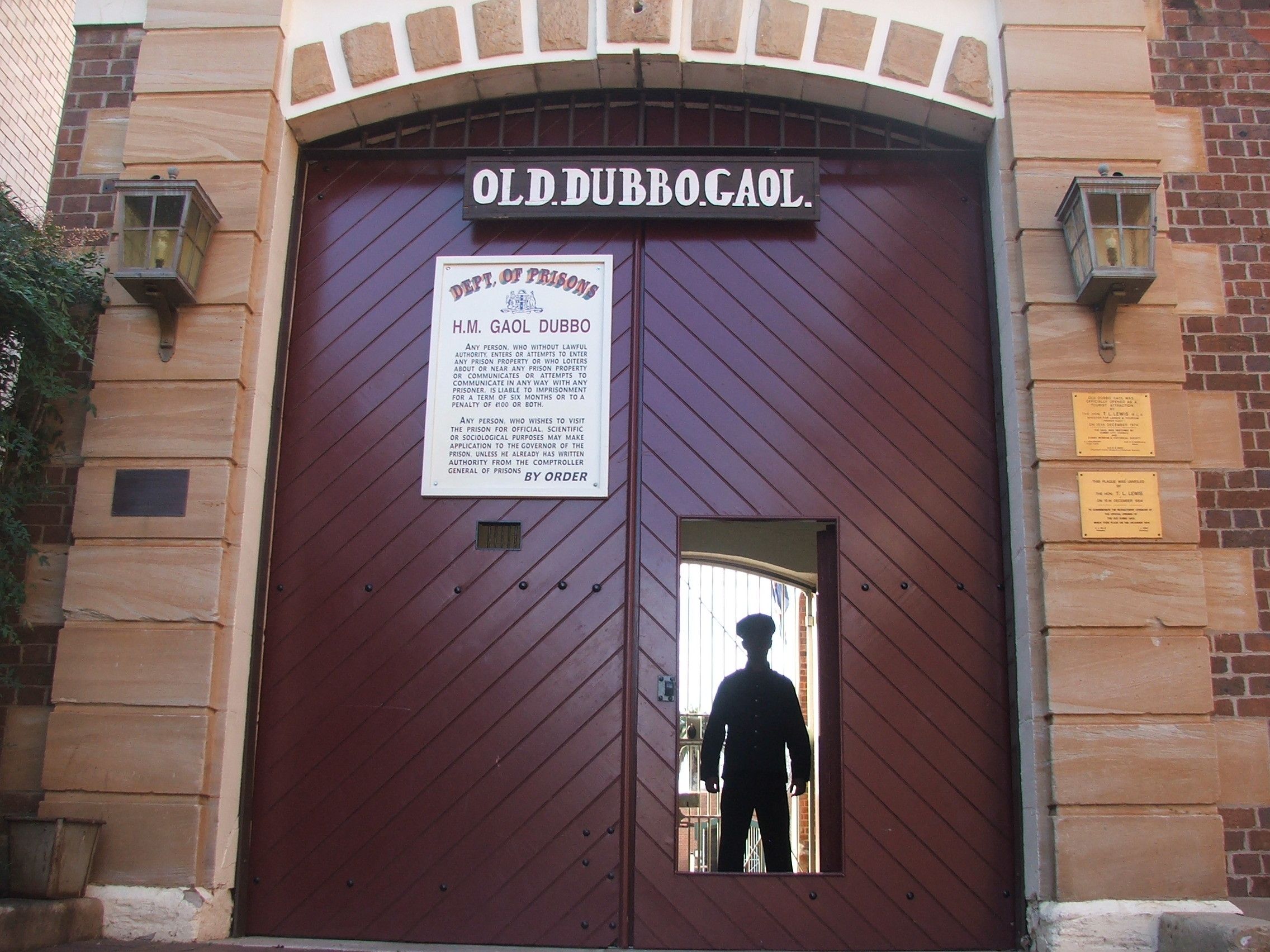 A large, arched entrance with a sign reading 'OLD DUBBO GAOL' and a notice about the Department of Prisons.