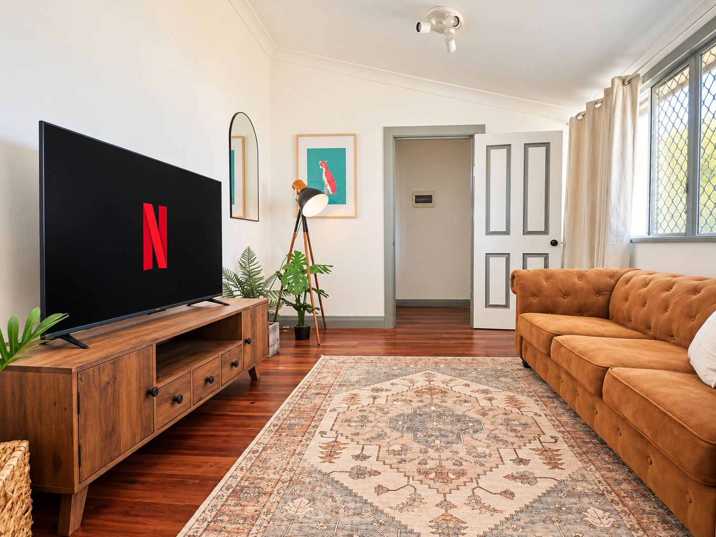 Ein Wohnzimmer mit Flachbildfernseher, braunem Sofa, einem gemusterten Teppich und einem Holzschrank.