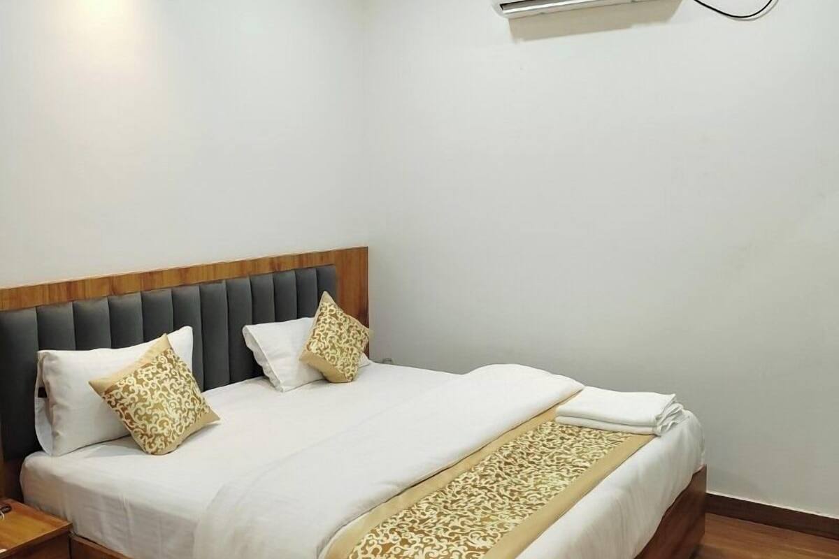A hotel room with a bed, a ceiling fan, an air conditioning unit, and wooden flooring.