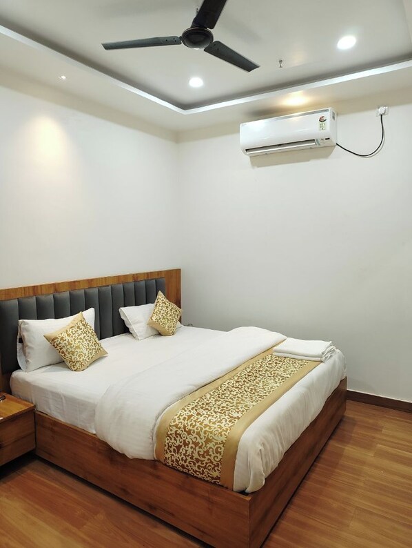 A hotel room with a bed, a ceiling fan, an air conditioning unit, and wooden flooring. - Kennedia International Hotel And Suites (Varanasi)