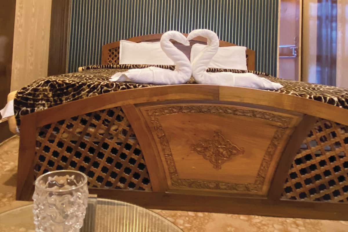 Quarto de hotel com cama de madeira, mesa de vidro com um copo de vidro transparente e parede listrada ao fundo.
