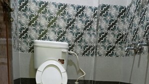 Ein Badezimmer mit Toilette, Eimer und gemusterten Fliesen.