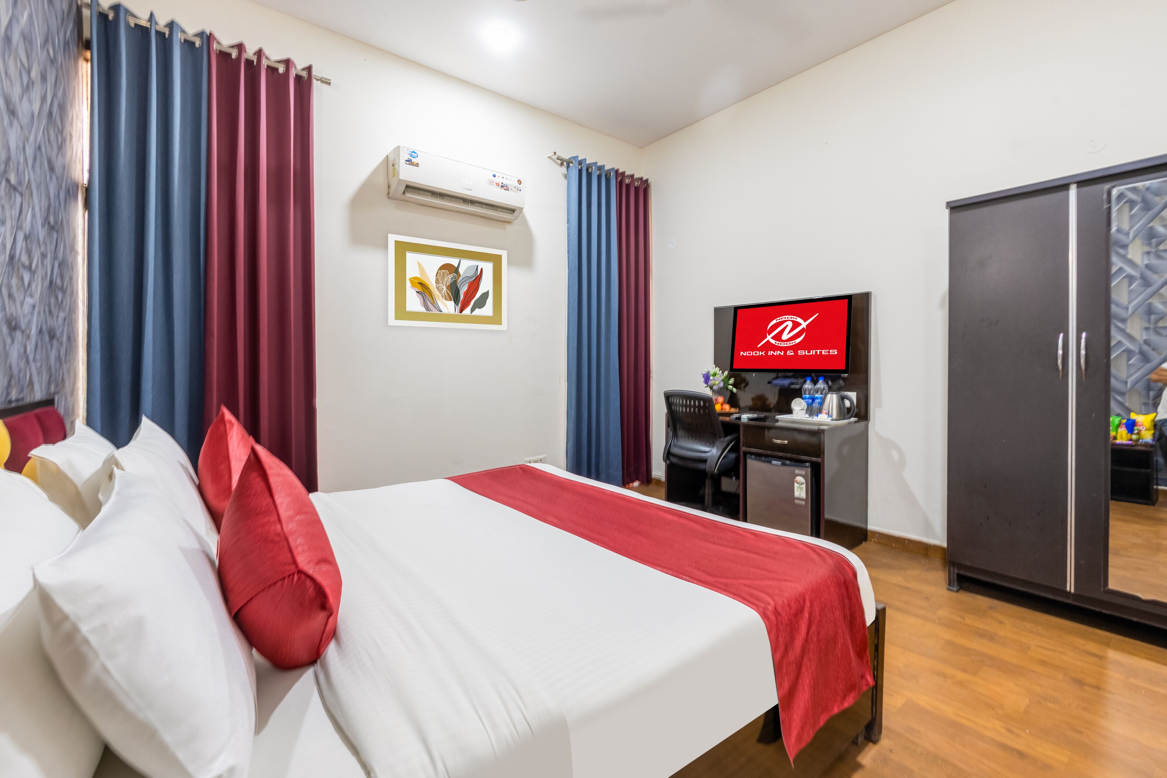 A hotel room with a bed, a desk with a computer, a television, and a wardrobe.