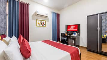 A hotel room with a bed, a desk with a computer, a television, and a wardrobe.
