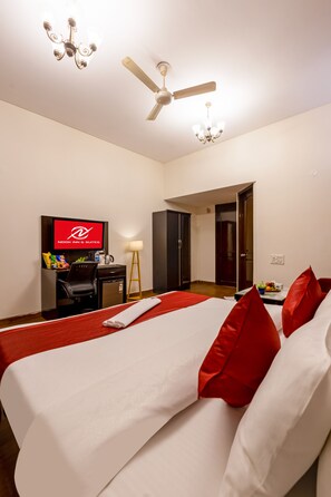 Una habitación de hotel con cama, escritorio, televisor, ventilador de techo y una puerta.