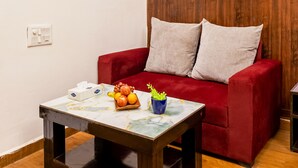 A red sofa with two pillows, a wooden coffee table with a fruit bowl and a vase, and a framed picture on the wall. - Nook Inn & Suites (Gurugram)