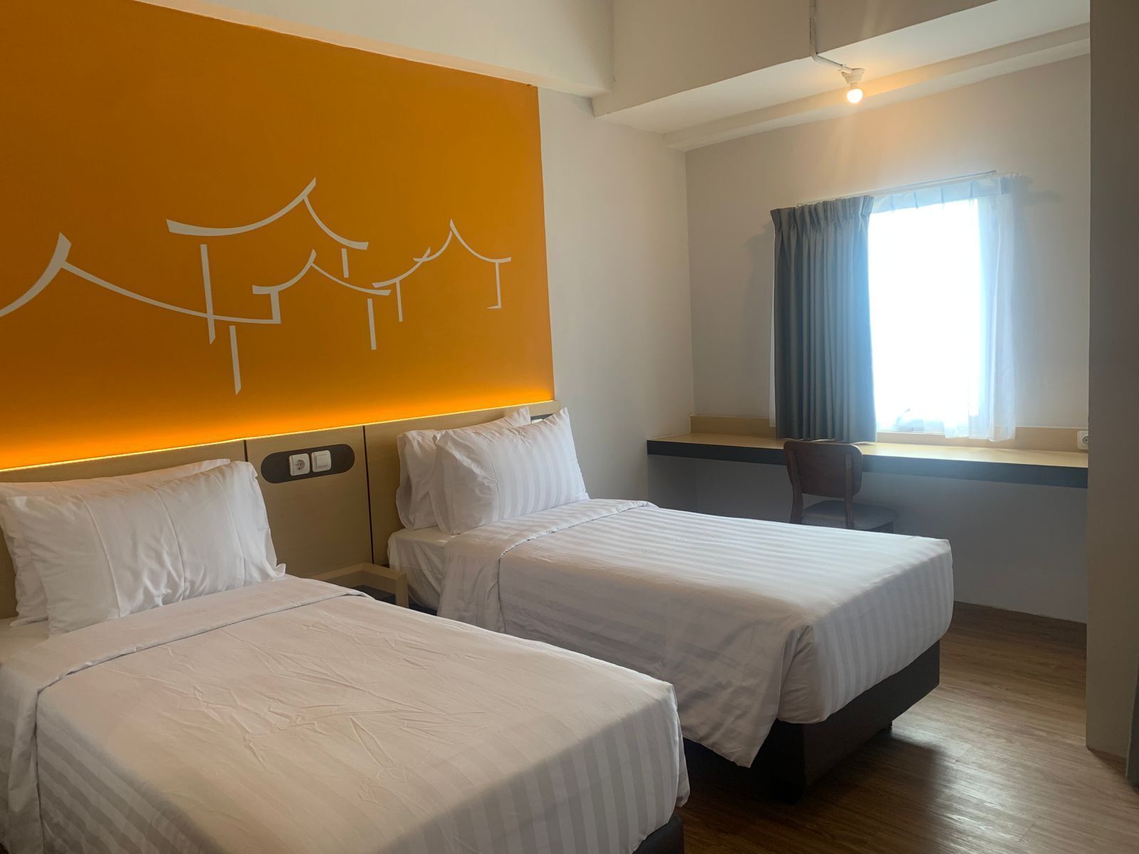 Ein Hotelzimmer mit zwei Betten, einem Schreibtisch und einem Fenster mit Vorhängen.