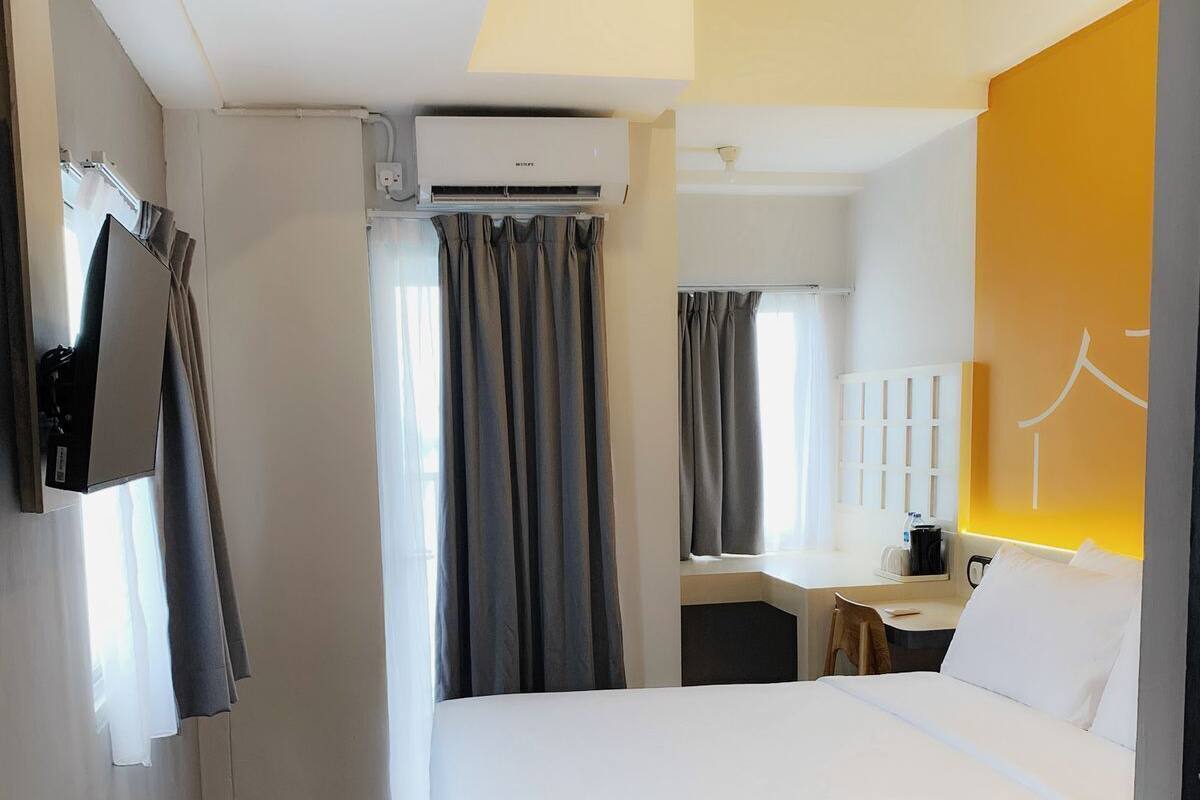 A hotel room with a bed, a desk, and an air conditioning unit.