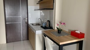 A compact kitchen with a sink, a kettle, and a small table with a chair. - Nemuru Stay BTC (Bekasi)
