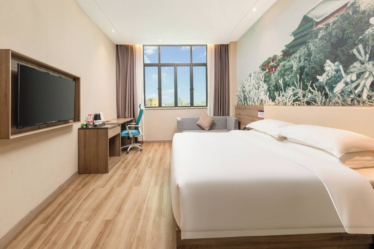 Une chambre d’hôtel dotée d’un grand lit, d’un bureau avec une chaise, d’un téléviseur à écran plat fixé au mur et d’une grande fenêtre donnant sur un immeuble.