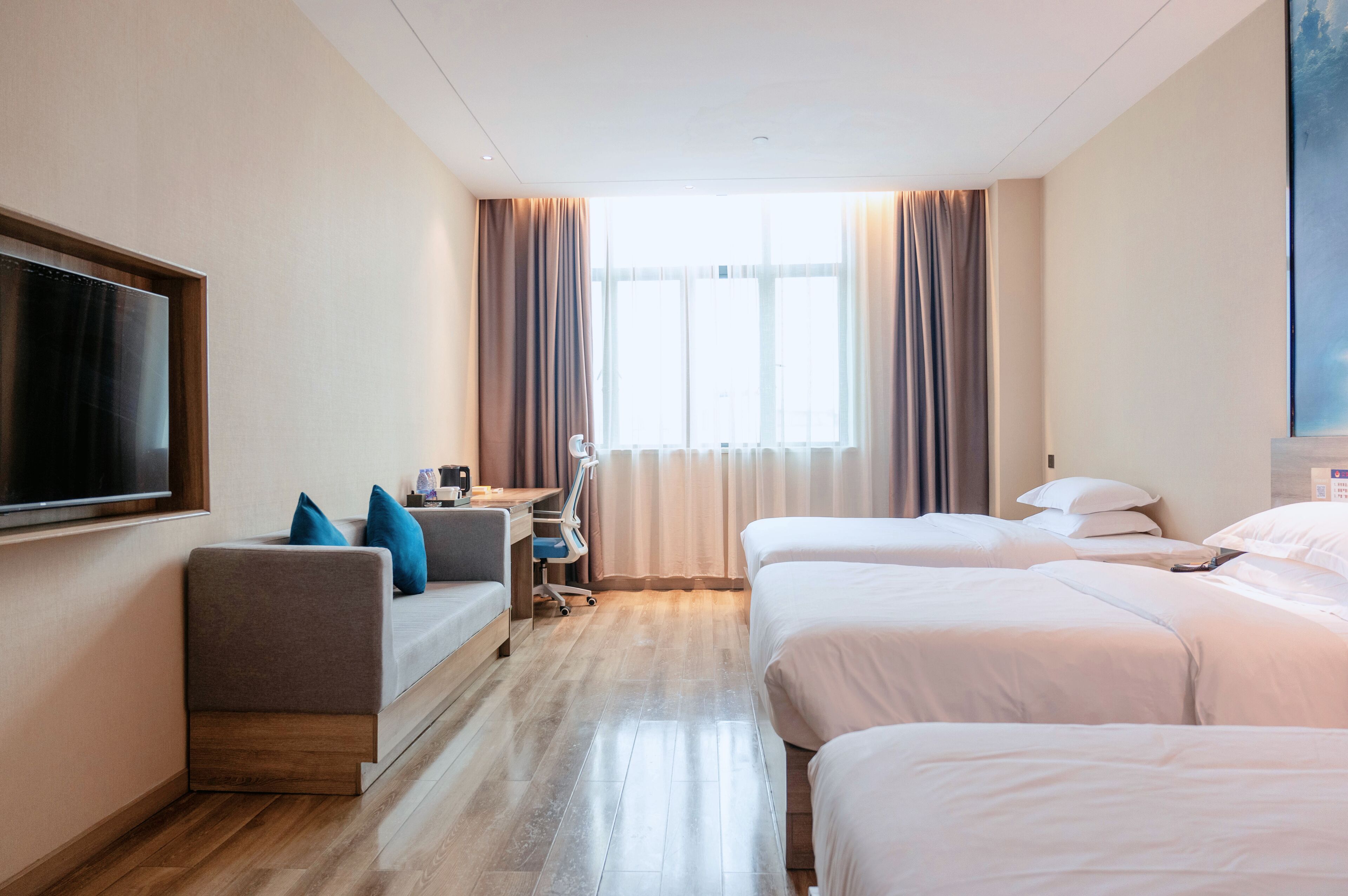 Quarto de hotel com sofá, duas camas, televisão e secretária com cadeira.