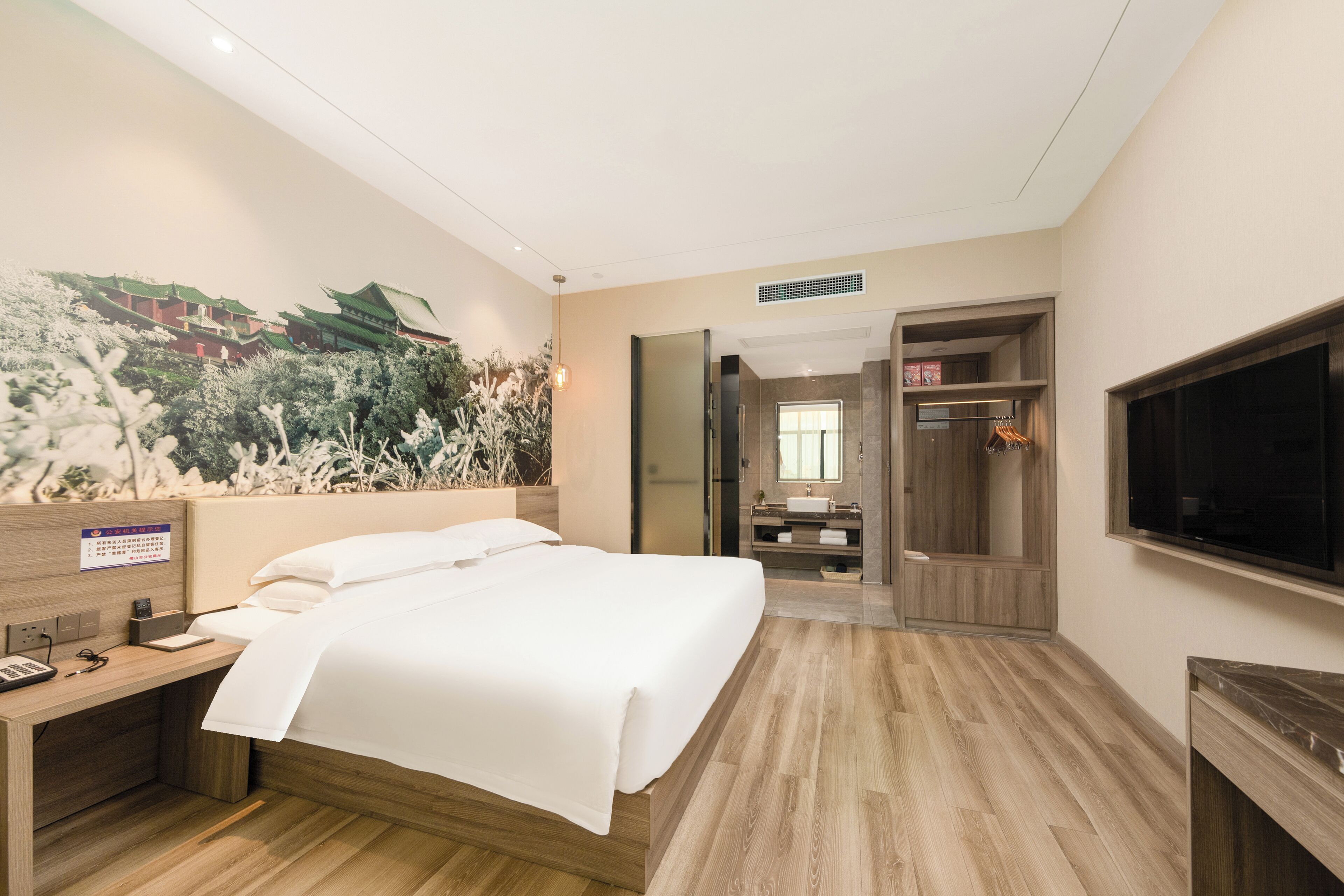 A hotel room with a bed, a desk with a phone, a TV, and a bathroom with a mirror and sink.