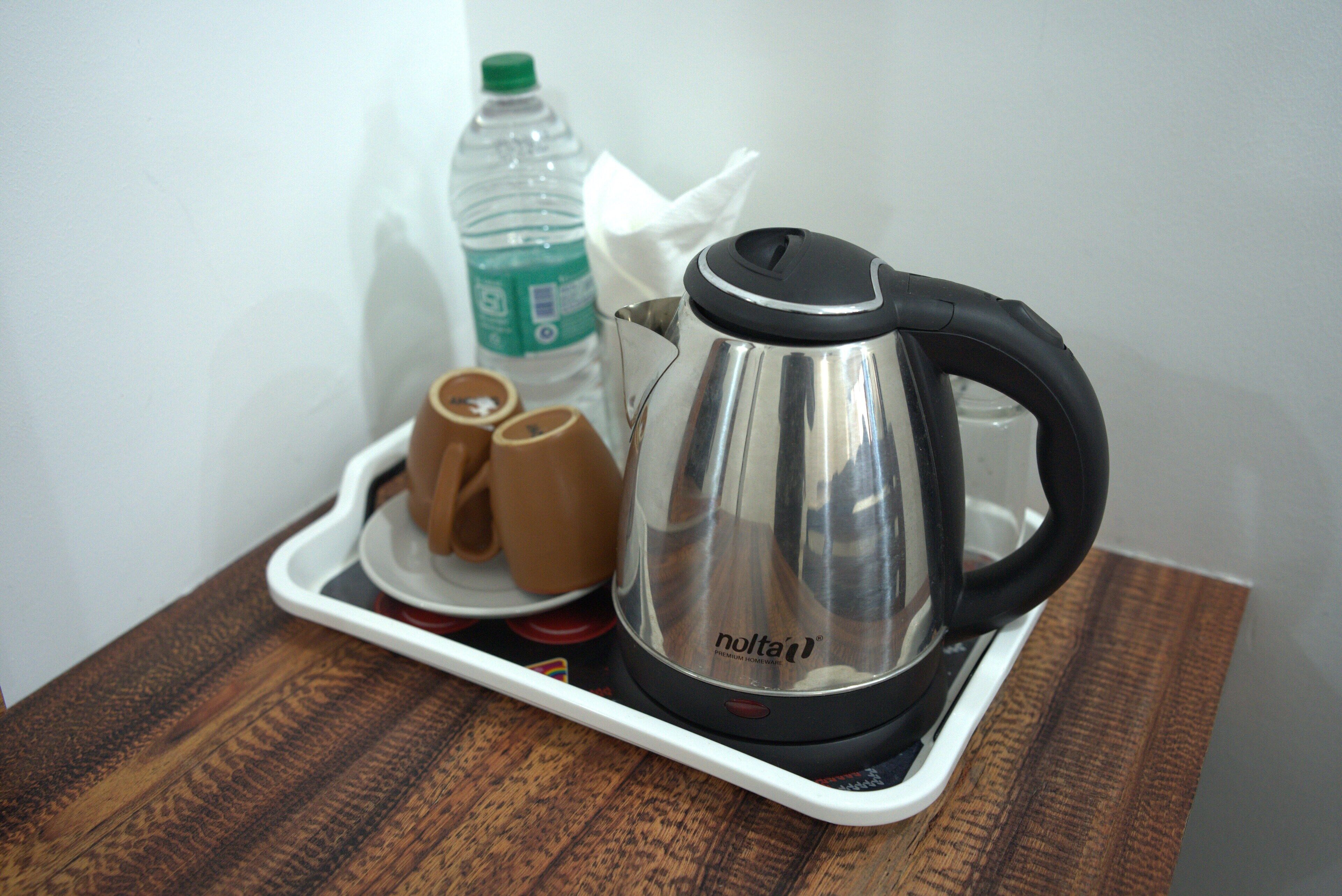 A tray with a stainless steel electric kettle, two brown cups, and a plastic water bottle on a wooden table.