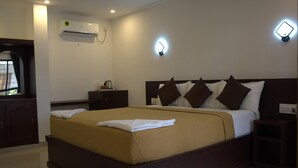 A neatly made bed with a brown headboard, a bedside table, and a wall-mounted air conditioner. - Puthooram Sea View Resort Varkala (Varkala)