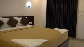 A hotel room with a bed, a nightstand, a wall clock, and a window with curtains. - Puthooram Sea View Resort Varkala (Varkala)