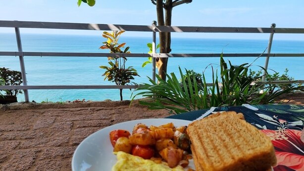 A plate of food with toast, eggs, and potatoes on a table with a view of the ocean. - Puthooram Sea View Resort Varkala (Varkala)