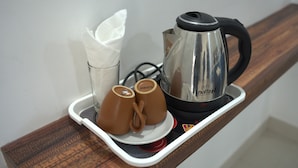 A tray with a stainless steel electric kettle, two brown mugs, and a white napkin holder on a wooden surface. - Puthooram Sea View Resort Varkala (Varkala)