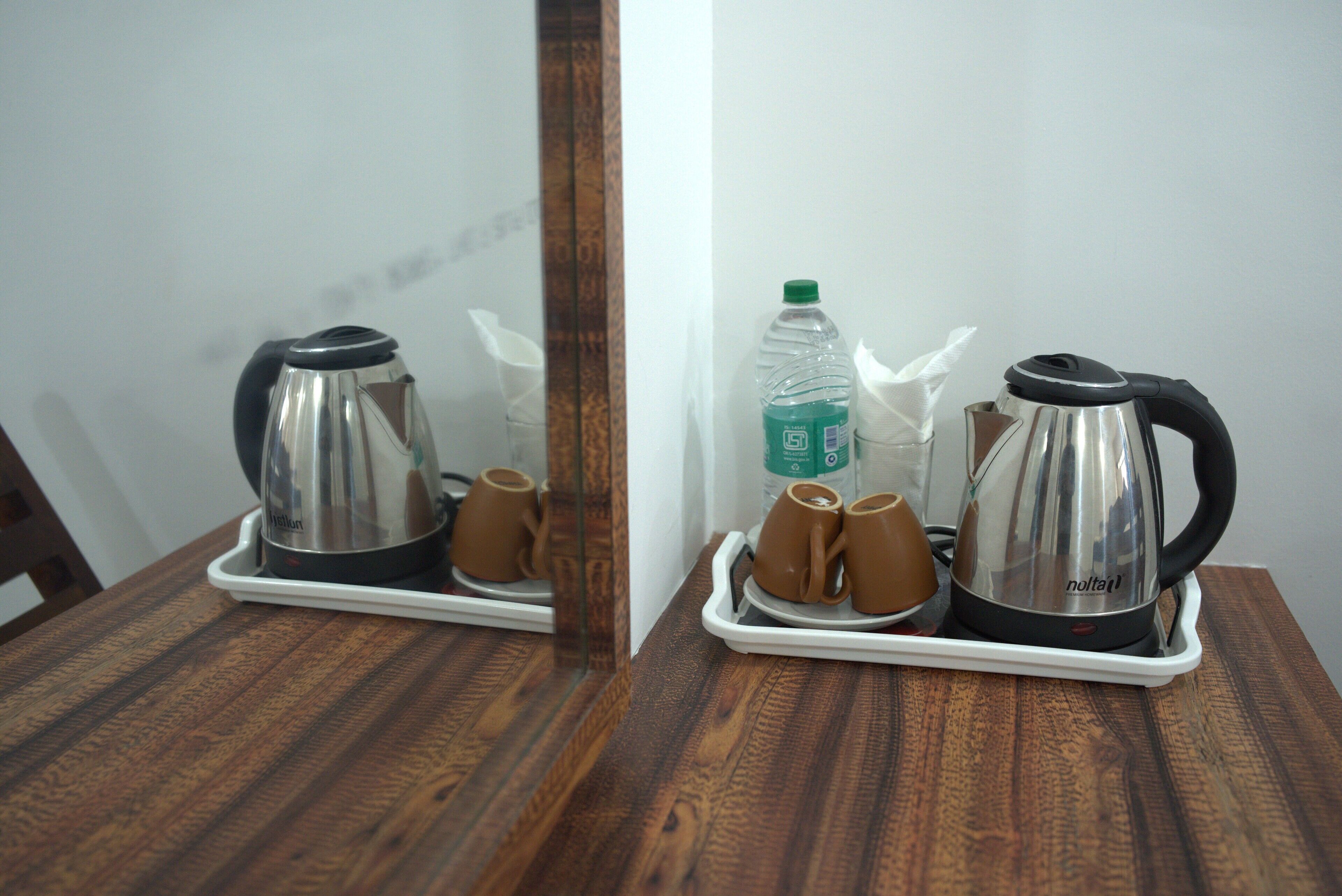A wooden table with a tray holding a kettle, two cups, and a bottle of water.