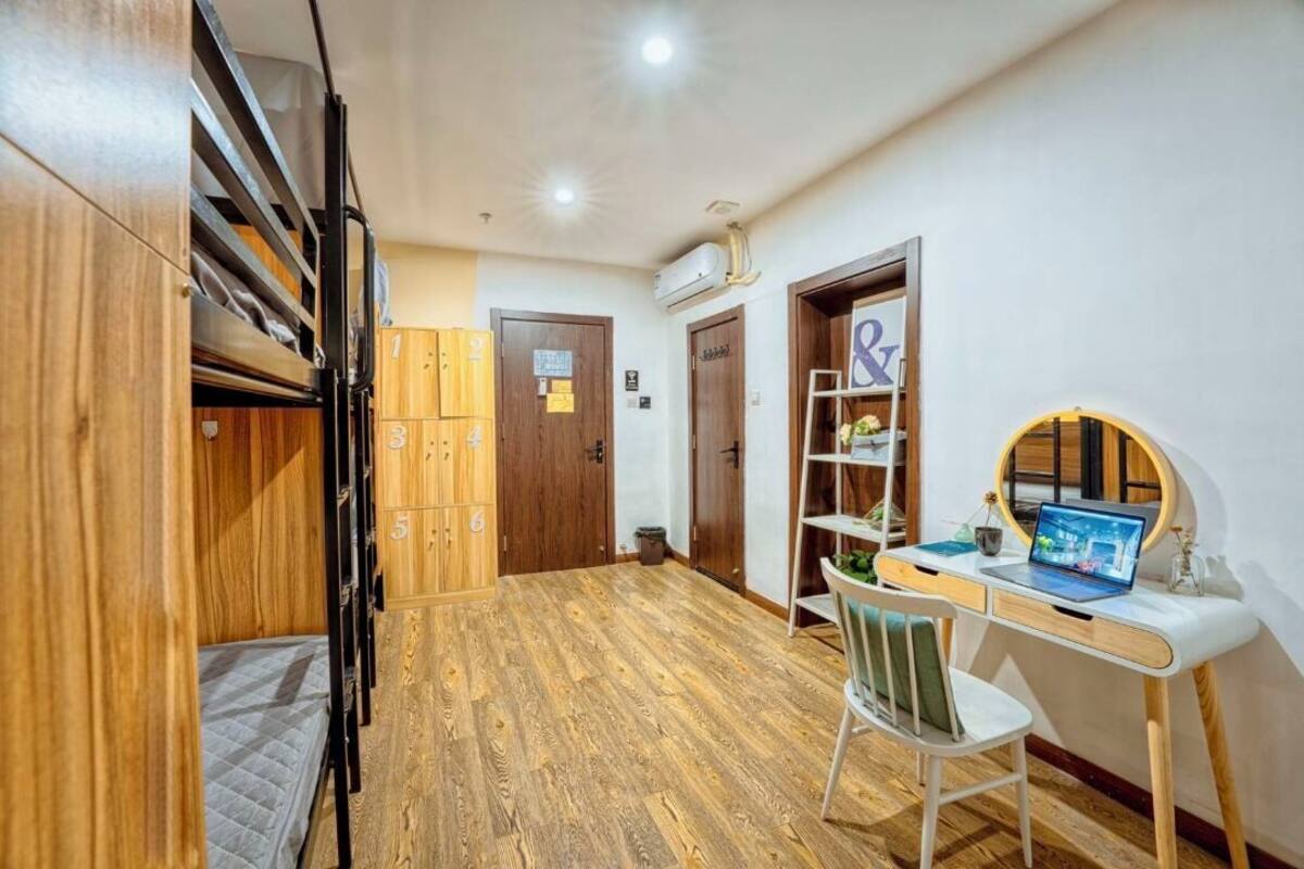 Una habitación de hotel con literas, un escritorio con una computadora portátil y un espejo redondo pequeño.