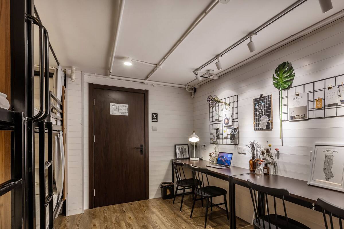 Una cocina moderna con suelo de madera, una puerta de madera oscura, y una pared blanca decorada con varios cuadros y una planta verde.