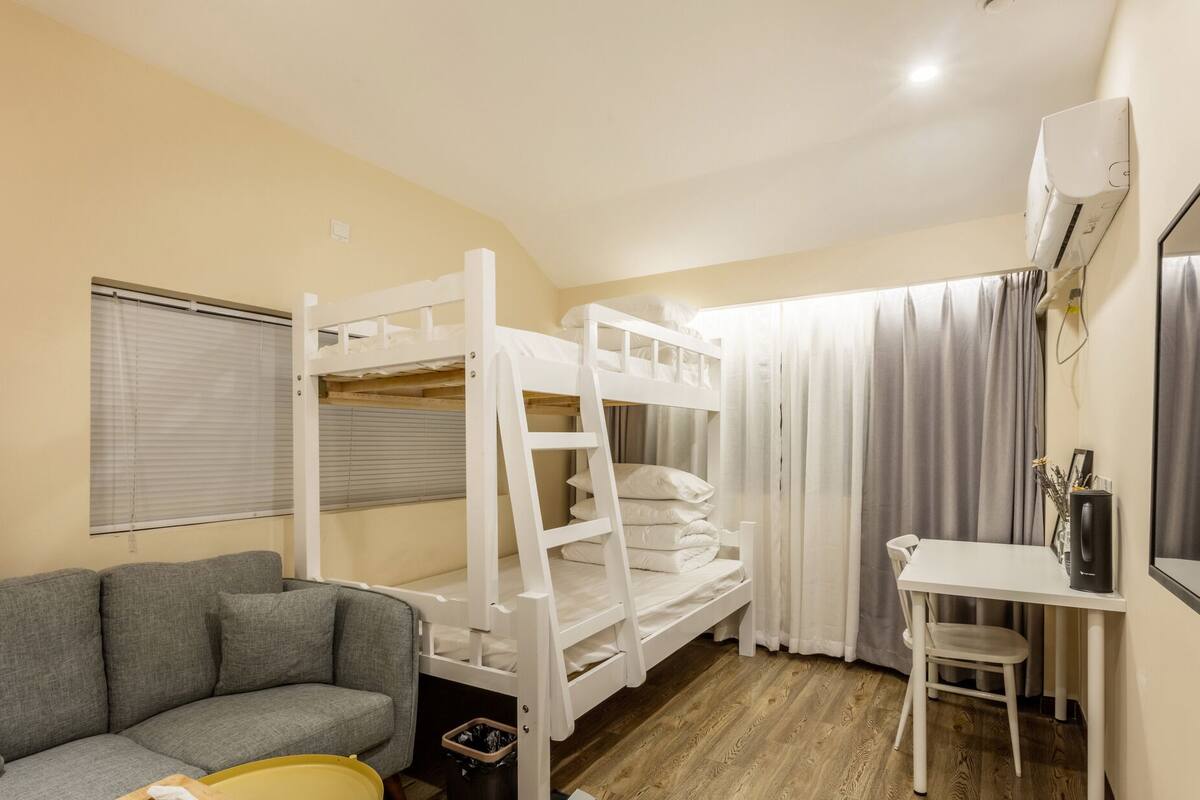Una habitación con una cama individual superpuesta, un sofá, una mesita y un escritorio.