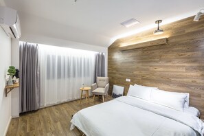 Ett hotellrum med en väggpanel i trä, en säng med vita sängkläder, ett litet runt bord, en stol och ett fönster med gardiner.