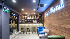 Una zona de bar con un letrero de neón, pared de madera, taburetes y una silla azul, además de un portátil sobre la barra.