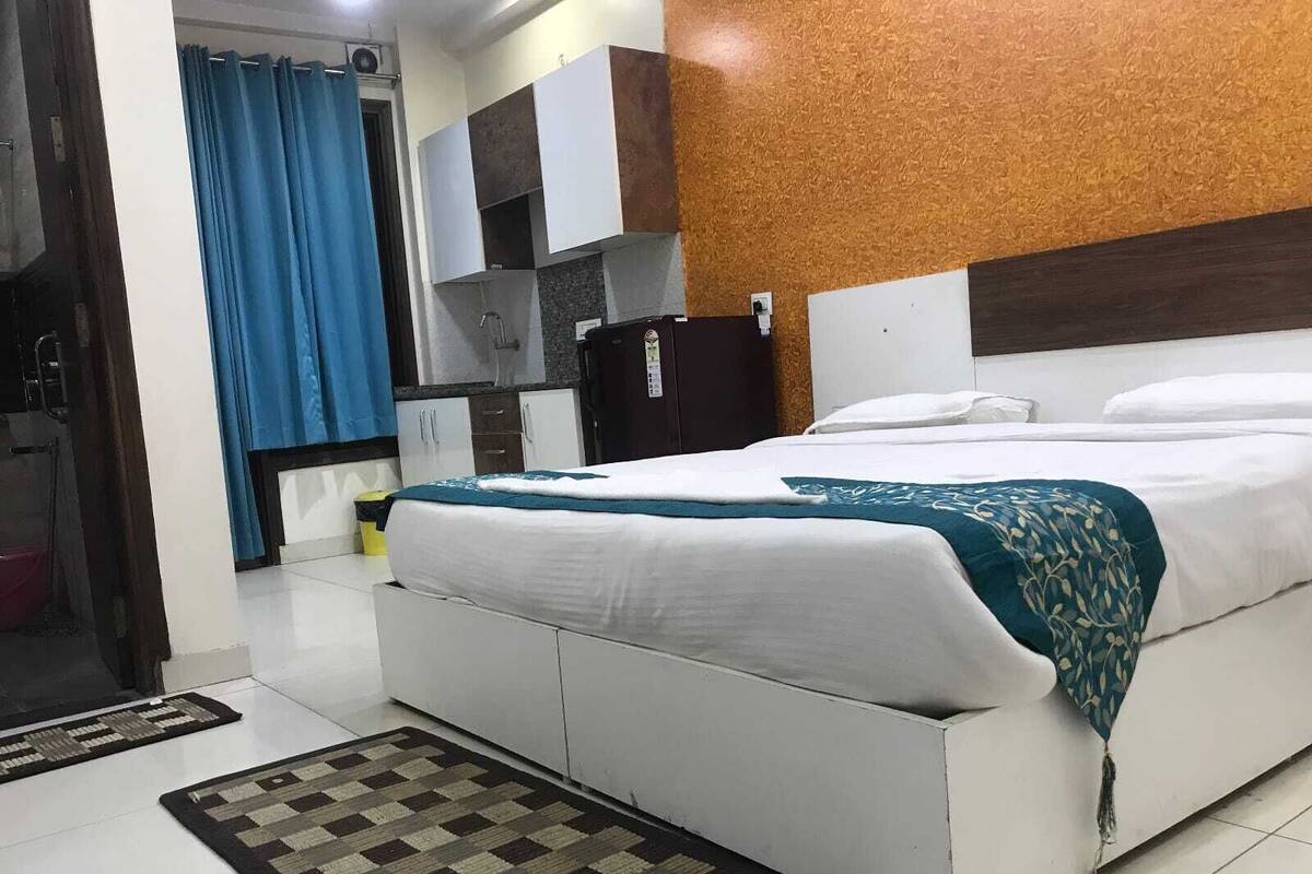 A hotel room with a bed, a small kitchenette, and a bathroom visible through an open door.