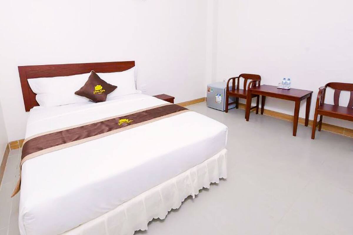 Une chambre d’hôtel comprenant un lit, un bureau, deux chaises, une petite table et un réfrigérateur.