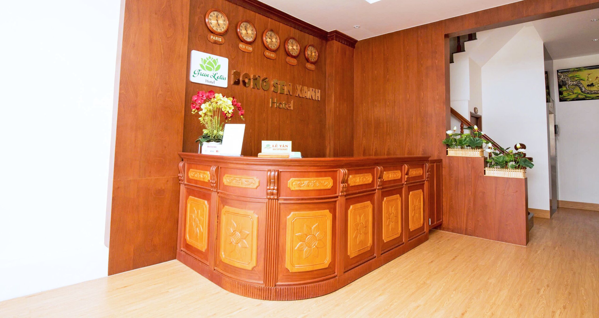 A wooden reception desk with clocks, a flower vase, and hotel signage.