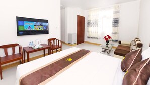Habitación de hotel con cama, televisión montada en la pared, escritorio con silla, una mesita con un florero y ventana con cortinas.