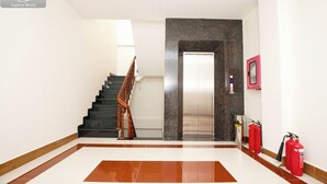 Un vestíbulo de hotel con una escalera, una pared de mármol, un ascensor y extintores.