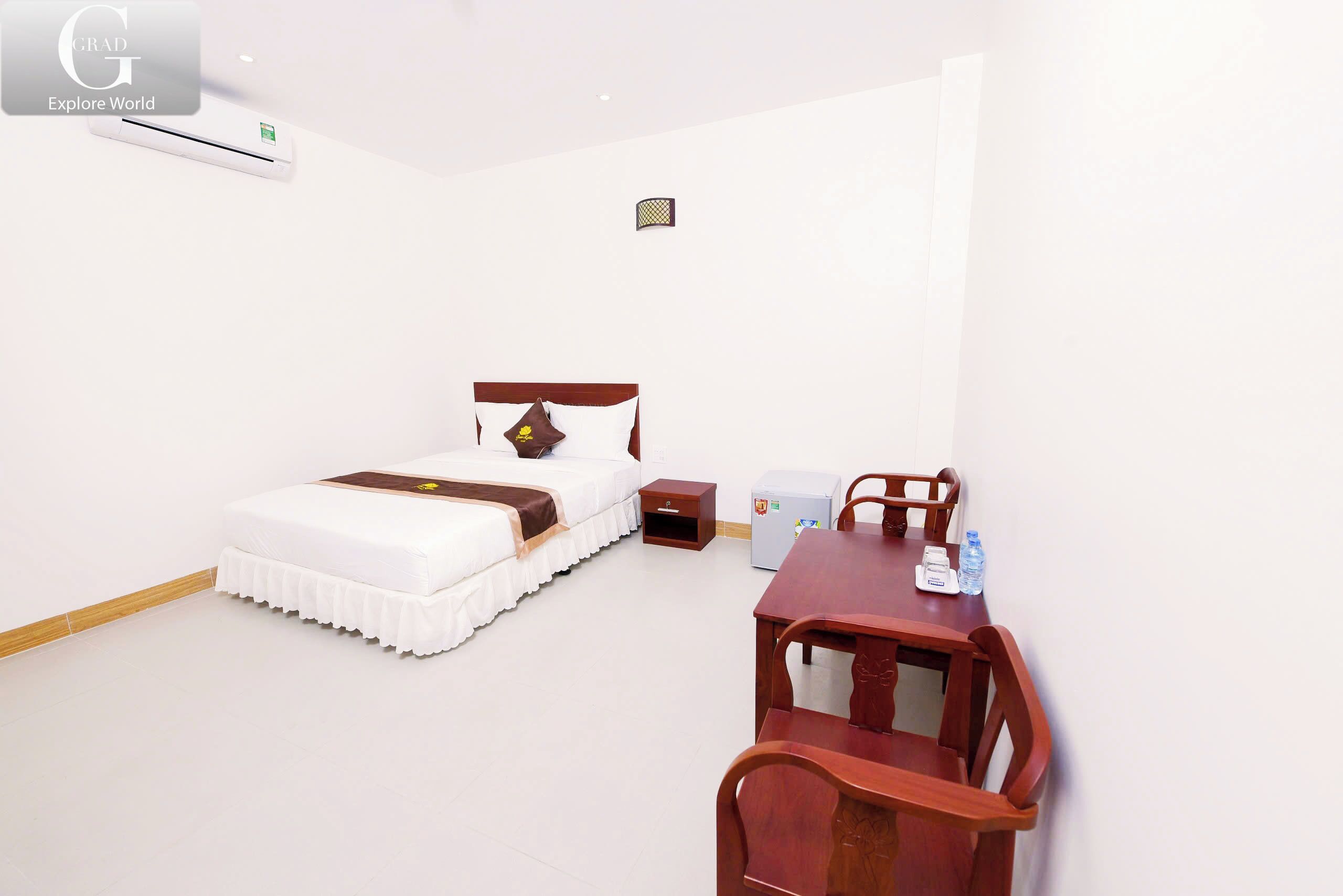 Habitación de hotel con cama, mesita de noche y escritorio de madera con sillas.