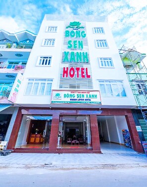 Een hotel met een groot bord waarop 'BONG SEN XANH HOTEL' staat en een kleiner bord eronder met 'GREEN LOTUS HOTEL'.